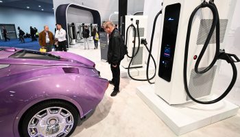 A man observes a purple luxury electric car next to a charging station at the Consumer Electronics Show in Las Vegas.