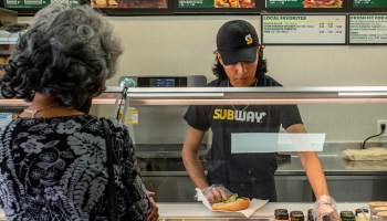 A customer orders at a Subway fast-food restaurant while a worker makes their sandwich.