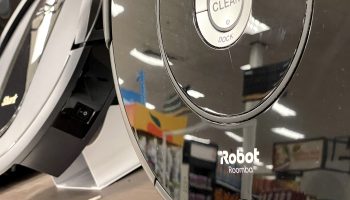 A black, disk-shaped Roomba robot vacuum made by the company iRobot is displayed on a shelf.