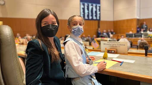 Representative Lara Cadena is joined by her child. Both are wearing masks that match their outfits.