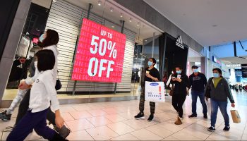 A group of masked shoppers walk past an Adidas store that has a red sign reading "Up to 50%."