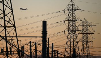 An aircraft takes off from LAX behind electric power lines at sunset.
