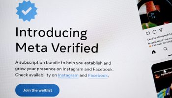This photo shows a close up on a phone screen. On the screen there's a blue check mark symbol and underneath black text that reads "introducing meta verified" under the text is a blue button that reads "join the waitlist"