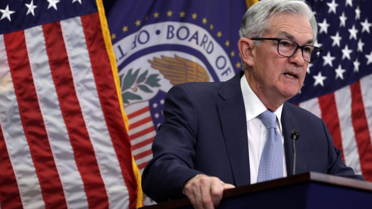 Federal Reserve Chair Jerome Powell stands at a lectern with American flags and the Fed seal behind him.