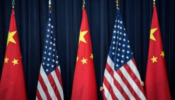 Against a background of dark blue curtains, three Chinese flags are in a row divided by American flags. The Chinese flags are bright red with yellow stars, and the U.S. flag has red and white stripes, with a blue block that contains 50 white stars.