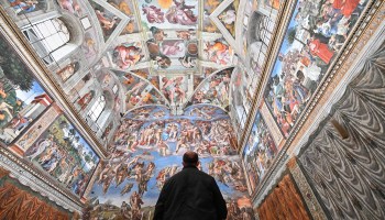 A lone figure looks up at the brightly painted ceiling of the Sistine Chapel.