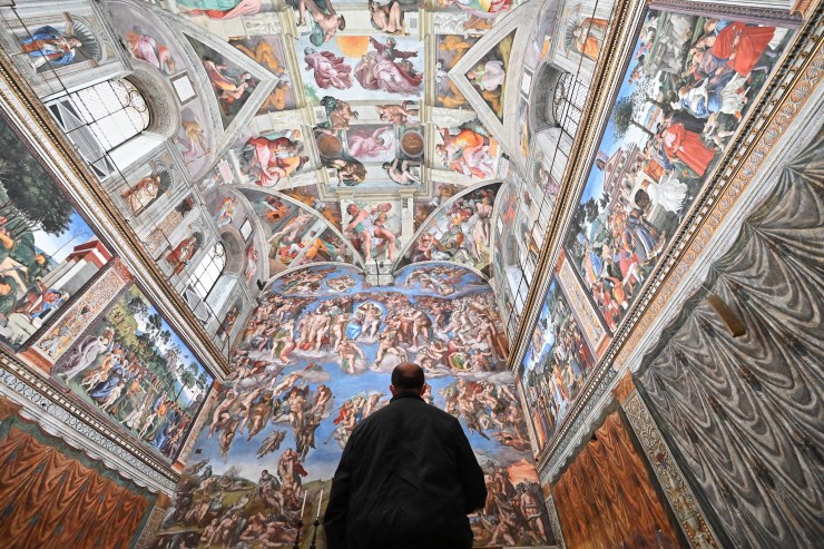 A lone figure looks up at the brightly painted ceiling of the Sistine Chapel.