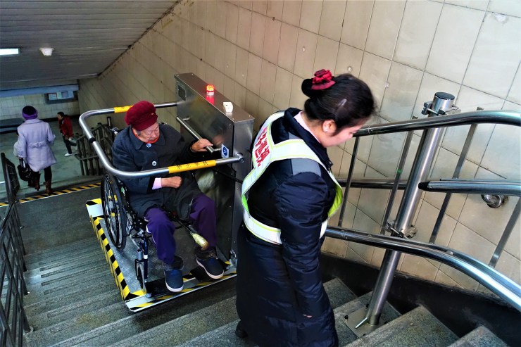 An elderly woman in a wheelchair riding a lift to go up a Shanghai subway staircase. The number of retirees is rapidly growing but there are fewer workers to fund for their care. (Charles Zhang/Marketplace)