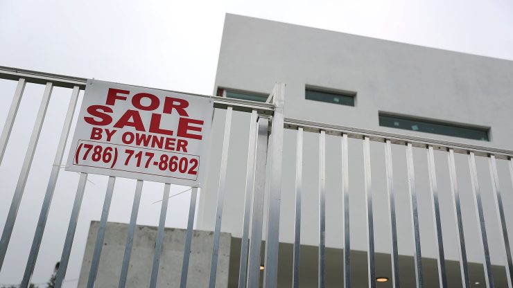 A for sale sign is posted on the silver fence of a modern house.