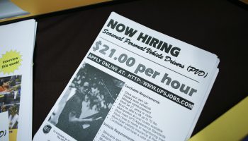 A flyer at a job fair for UPS reads "Now Hiring Seasonal Personal Vehicle Drivers. $21.00 per hour."