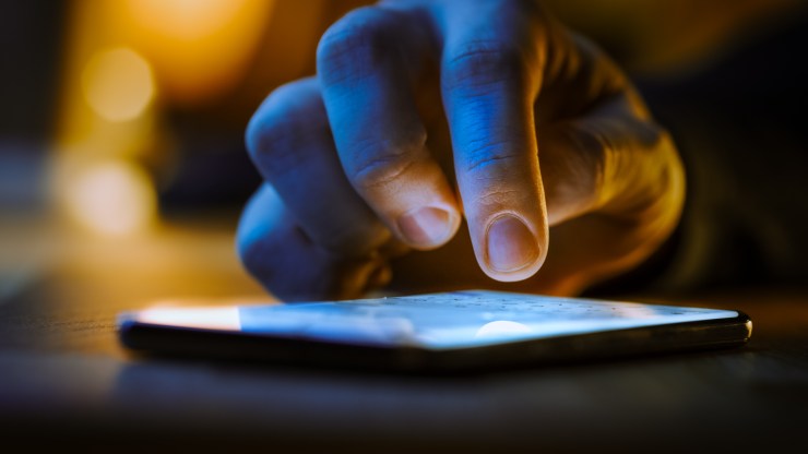 A close up image of a person's hand hovering over a glowing smart phone.