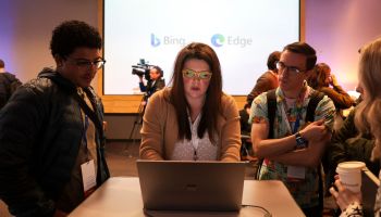 Three people lean over a computer to see a demonstration of Microsoft's AI-powered Bing search engine.