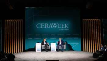 Two men in dark suits sit on a stage underneath a sign that reads "CERAWEEK by S&P Global." The silhouettes of audience members' heads are in the foreground.