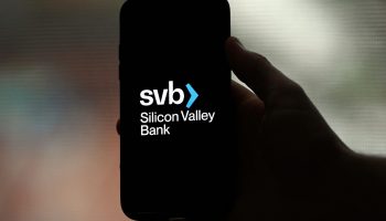 A hand is seen holding a phone with a black screen that reads "svb> Silicon Valley Bank."