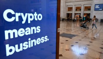 A woman walks past a sign advertising cryptocurrency banking at Union Station in Washington, DC. The sign is blue and in white lettering reads "crypto means business"