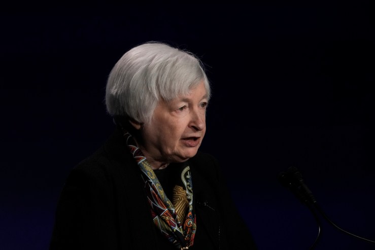 Treasury Secretary Janet Yellen is in profile, facing right. She's wearing black, except for a colorful scarf around her neck. Her face, white hair and scarf are in contrast to the rest of the frame, which is filled with black, so that she appears floating.