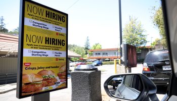 A "Now Hiring" sign is displayed on a digital screen in a McDonald's drive-thru.