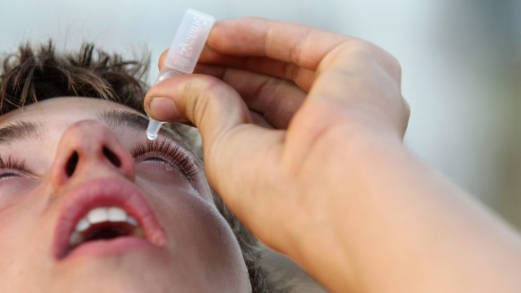 A person uses eye drops.