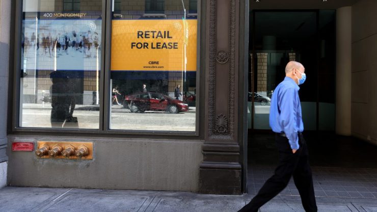 A pedestrian walks by yellow sign that says, "Retail for Lease" on a commercial property in San Francisco, California.