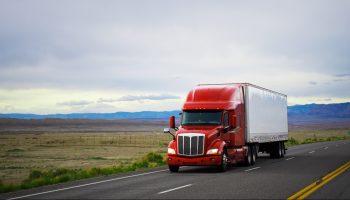 Red and white semi-truck drives through the plains of Utah.