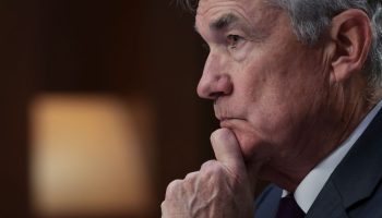 Fed Chair Jerome Powell, a man with gray and white hair, sits in profile with his mouth closed and his chin resting in his left hand.