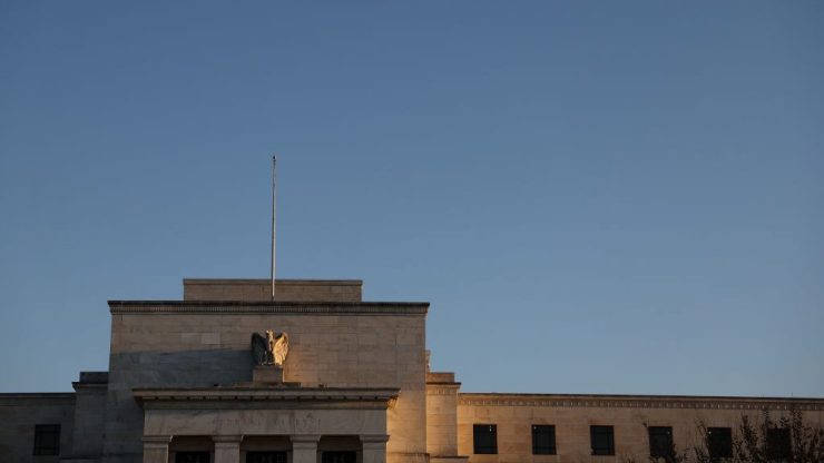 The top of the Federal Reserve headquarters' block exterior against a blue sky. Near the top center of the building is an eagle sculpture.