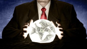 A businessman is consulting a crystal ball to foretell the future of the economy. There are 100 dollar bills floating in the crystal ball. The businessman is wearing a suit with a red tie. There is a blue glow in the background.
