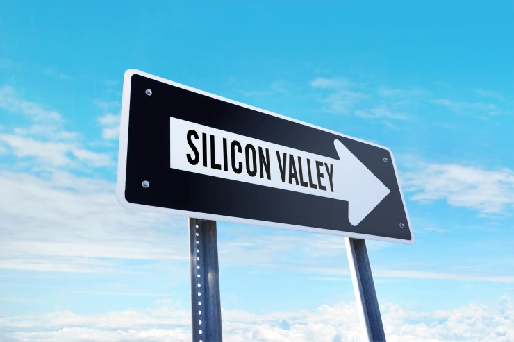 "Silicon Valley" is written in black letters on a white right-facing arrow. The arrow is part of a black traffic sign. In the background, a few white clouds drift across a blue sky.