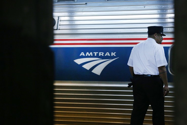 A train conductor stands next to an Amtrak train.