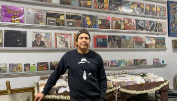 A man stands in front of a wall of vinyl records.