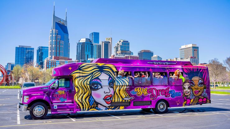 A colorful bus that reads "The Big Drag Bus" is parked in a parking lot set against the Nashville skyline.