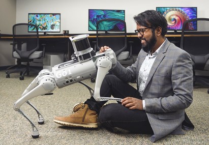 Purdue University professor Aniket Bera sits on the floor to pet a dog-like robot.