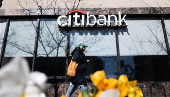 A woman walks past a Citibank branch behind a row of yellow tulips.