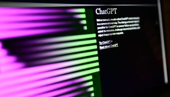 A computer shows the home screen of the OpenAI website: In the upper right corner in white lettering is the word "ChatGPT" with text underneath it. To the left, stripes of purple fade to green as they reach the right side. The background is black.