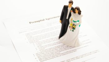 Bride and groom cake-topper sits on top of written out prenuptial agreement paper.