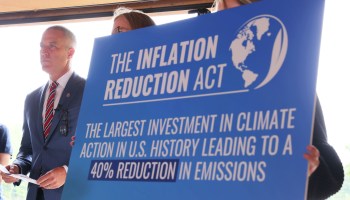 Lawmakers stand next to a poster that reads "The Inflation Reduction Act. The largest investment in climate action in U.S. history leading to a 40% reduction in emissions."