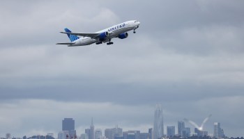 A United Airlines plane taking off in cloudy weather with the San Francisco skyline in the background.