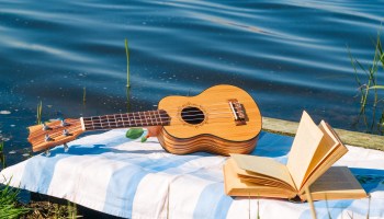 A ukulele and an open book rest on a cloth near a body of water.