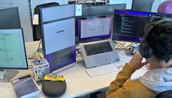 An ITJuana engineer works on a project with a San Diego-based biotech company. The engineer is wearing headphones and has several monitors open on a desk.