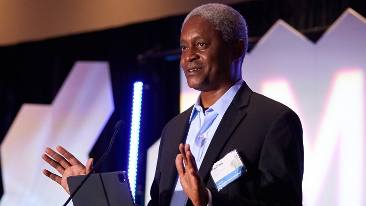 Raphael Bostic, president and CEO of the Federal Reserve Bank of Atlanta, speaks at a conference wearing a black suit and blue button-up shirt.