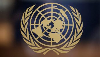 The United Nations logo is seen in gold on a glass window. It is a globe, seen from the north pole.