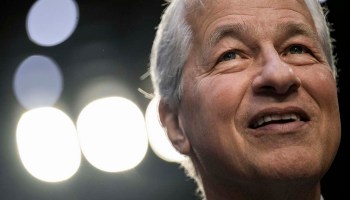 JPMorgan Chase CEO Jamie Dimon's face is seen in a closeup shot with bright lights shining behind him in an otherwise darkened room.