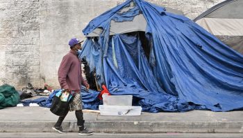 A person walks past a tattered blue tent for the homeless in Los Angeles, California.
