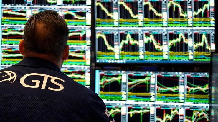 The back of the stock trader's head can be seen in front of screens showing stock charts.