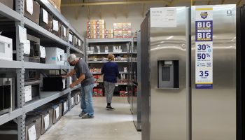 Two customers shop in a microwave aisle at a store selling appliances.