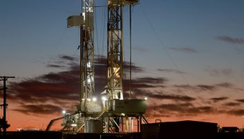 An oil drilling rig with lights on setup in the Permian Basin oil field in Midland, Texas with a dark blue and pink sky surrounding it.