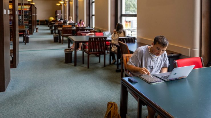 Students work at tables situated in a college library.