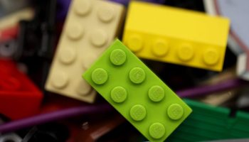 In a bin of Lego bricks, a lime green lego is stacked on a cream- and yellow-colored one.