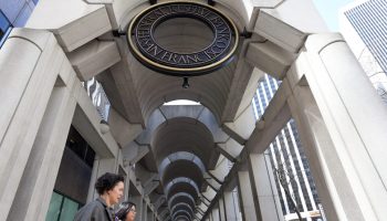 Two women walk past arches and the bronze, circular sign for the Federal Reserve Bank of San Francisco on March 16.