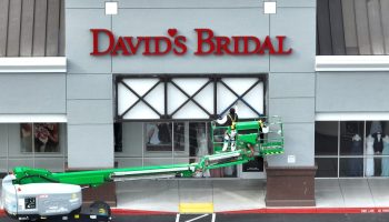 A painter in a boom lift paints the store front of a David's Bridal shop.